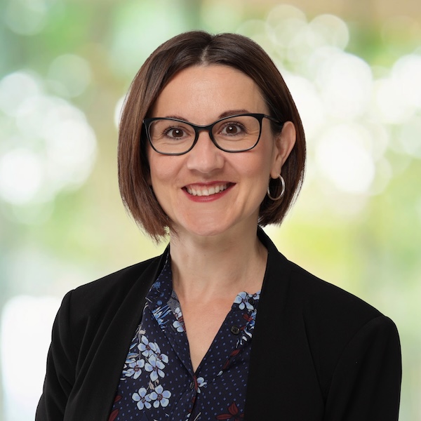 Porträt von Natasa Knezevic mit Brille, kurzem braunem Haar und floral gemusterter Bluse vor hellem, unscharfem Hintergrund
